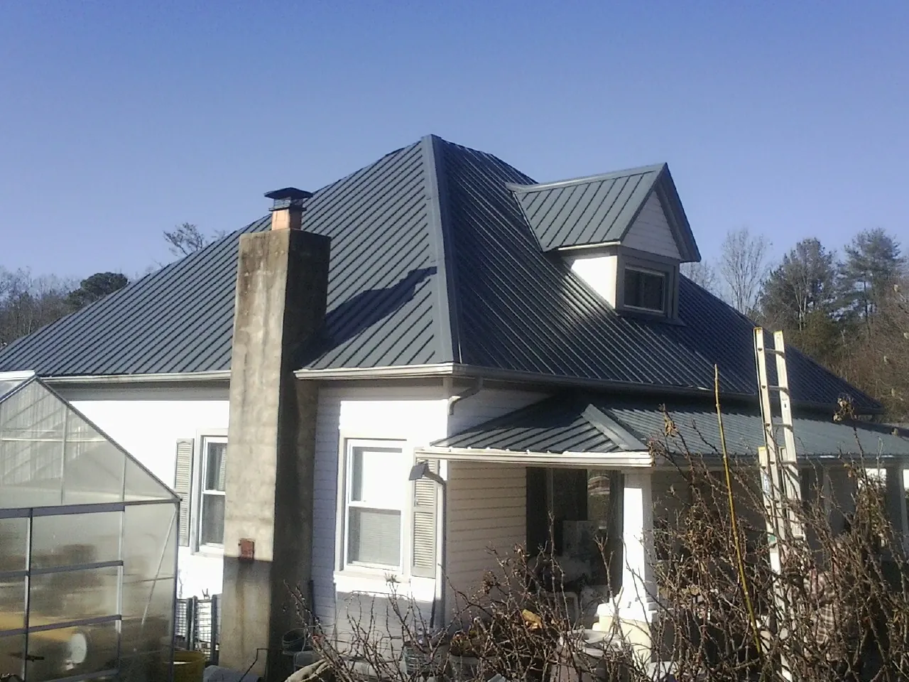 Dark blue standing seam metal roof on a white farmhouse with dormer — Slate & Tile Roof Repair by Roofing Brothers in Bear Creek