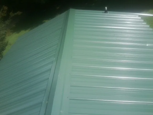 New green metal panels meeting at the ridge of a roof — Flat Roof Repair work by our crew in Bear Creek