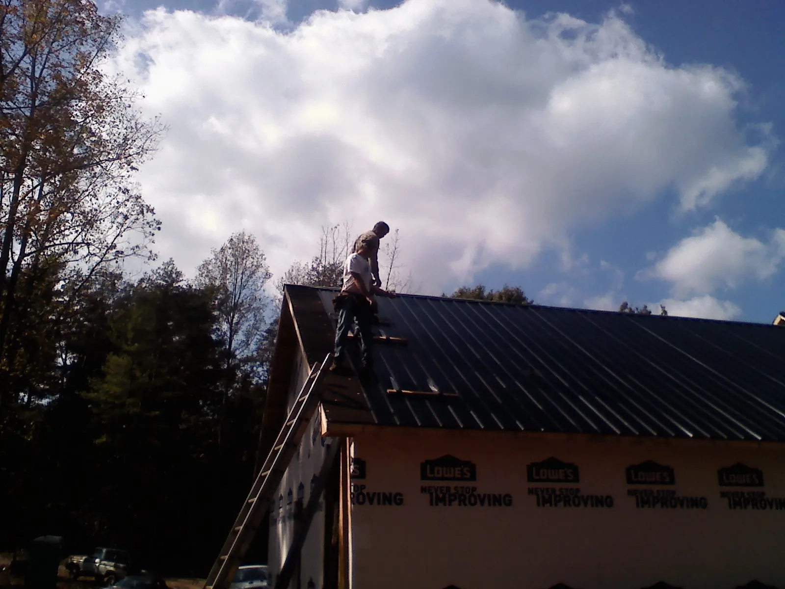 Roofer fastening dark metal panels high against a cloudy sky, from a Roof Inspection job in Bear Creek